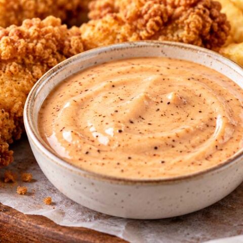 Homemade copycat Raising Cane's Sauce in a small bowl with crispy chicken tenders and golden French fries.